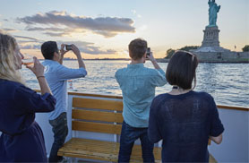 four people, taking photos of the statue of liberty across the water